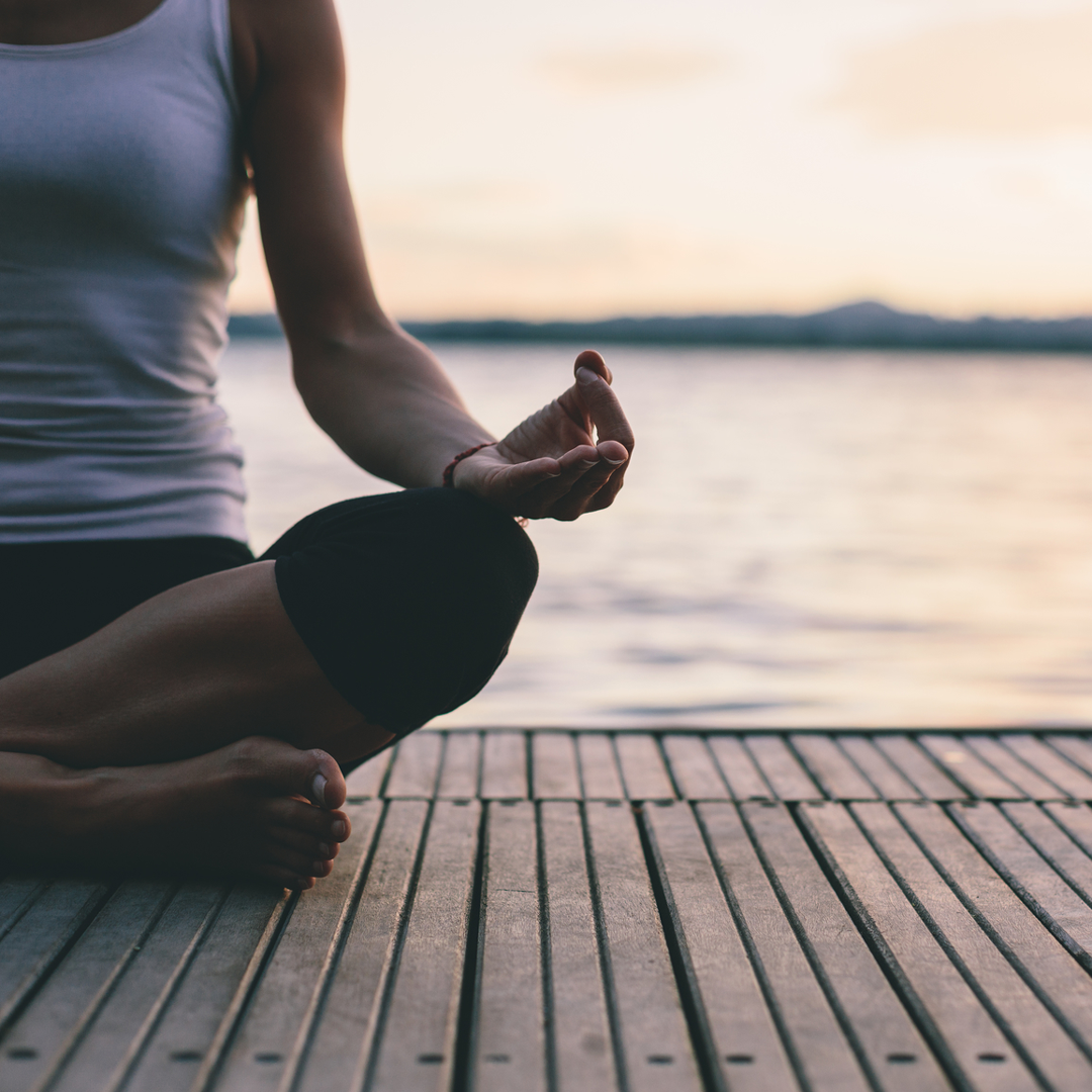 Image of woman sitting on a dock over the water meditating